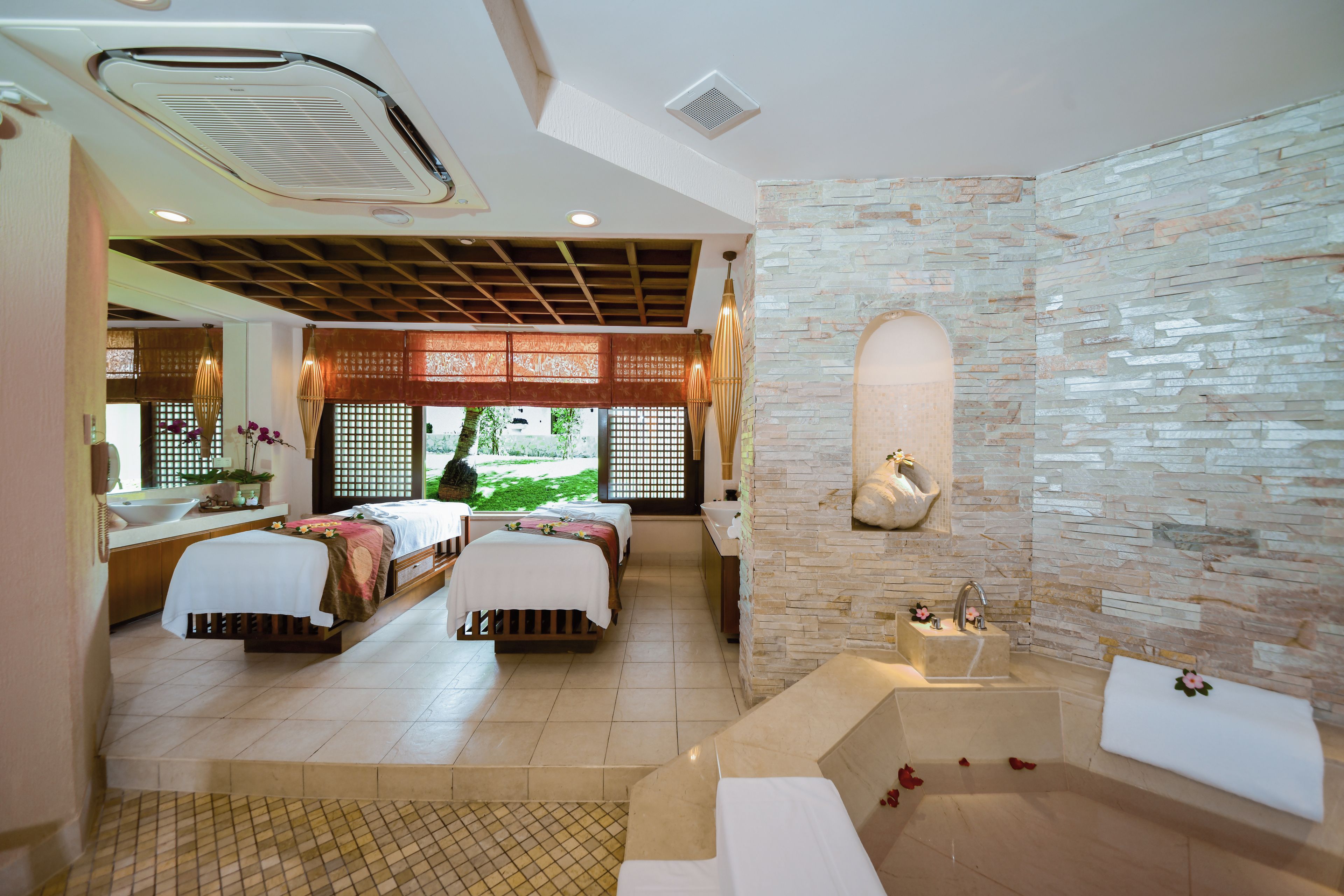 Habitación de hotel con dos camas, una bañera y una pared de piedra.