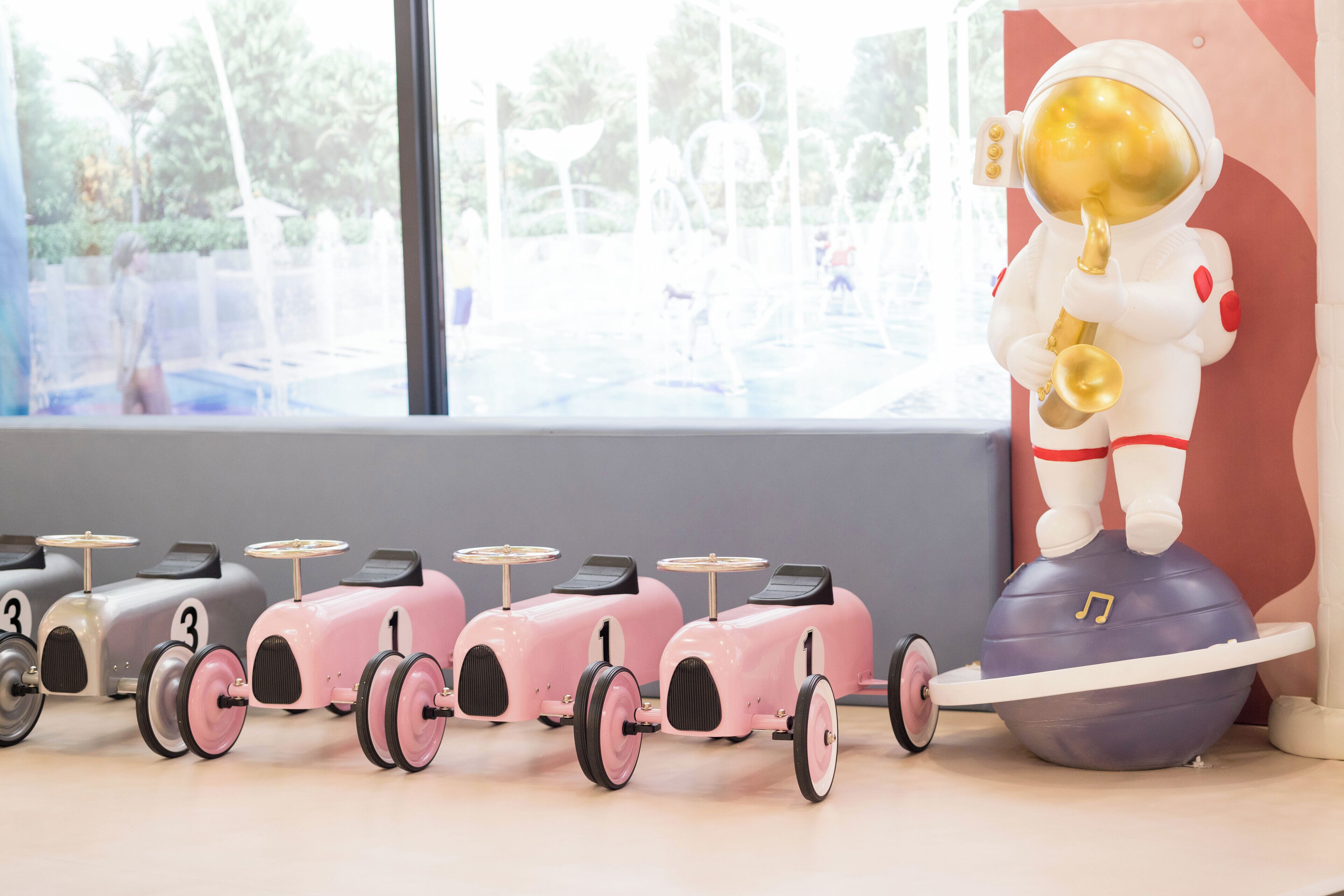 A row of vintage toy cars with numbers 1 to 3, a toy astronaut playing a saxophone, and a large blue ball with a music note.