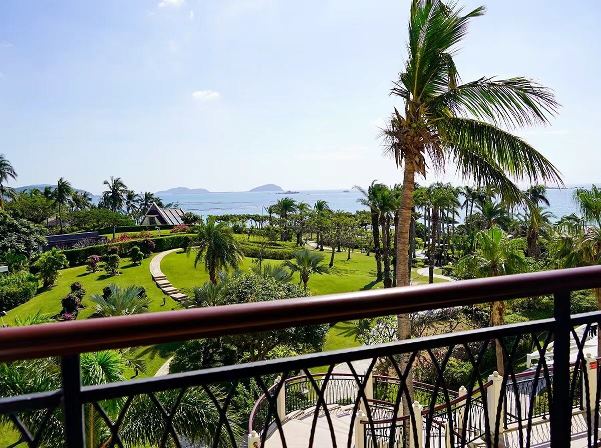 Un balcón con vistas a un jardín ajardinado, palmeras y el océano.