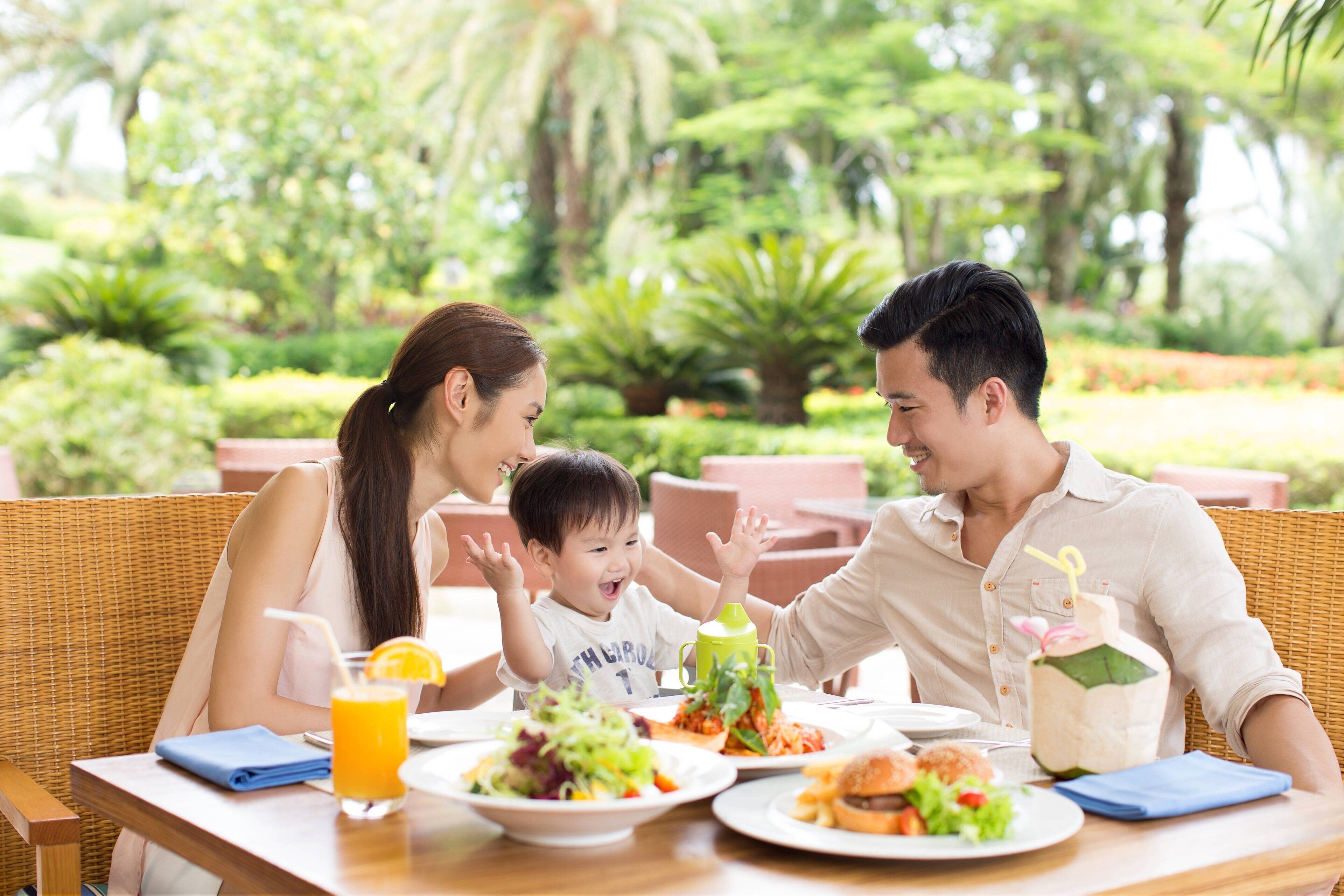 Una familia cenando al aire libre, con una mesa preparada para la comida, rodeada de exuberante follaje.