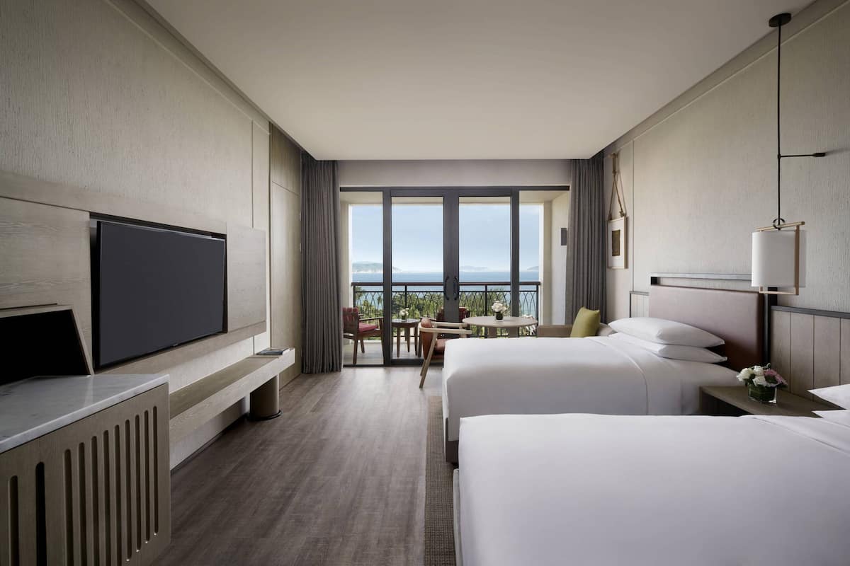 Une chambre d’hôtel avec deux lits, une télévision, un balcon avec vue et un coin repas.