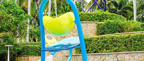 A pool with a water slide, a chair, and a decorative structure in the background.