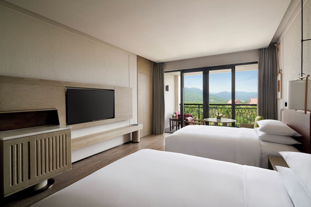 Une chambre d’hôtel avec deux lits, une télévision et un balcon offrant une vue sur les montagnes.