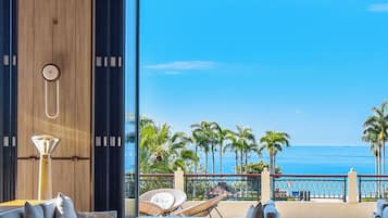 Un interior moderno con un amplio ventanal con vistas a una playa, amueblado con un sofá, sillas y una mesa.