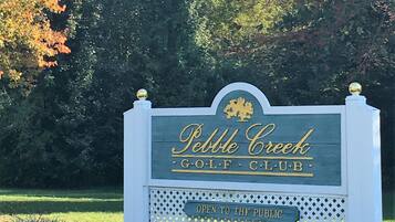 A sign for Pebble Creek Golf Club with a gold emblem and the text "OPEN TO THE PUBLIC".