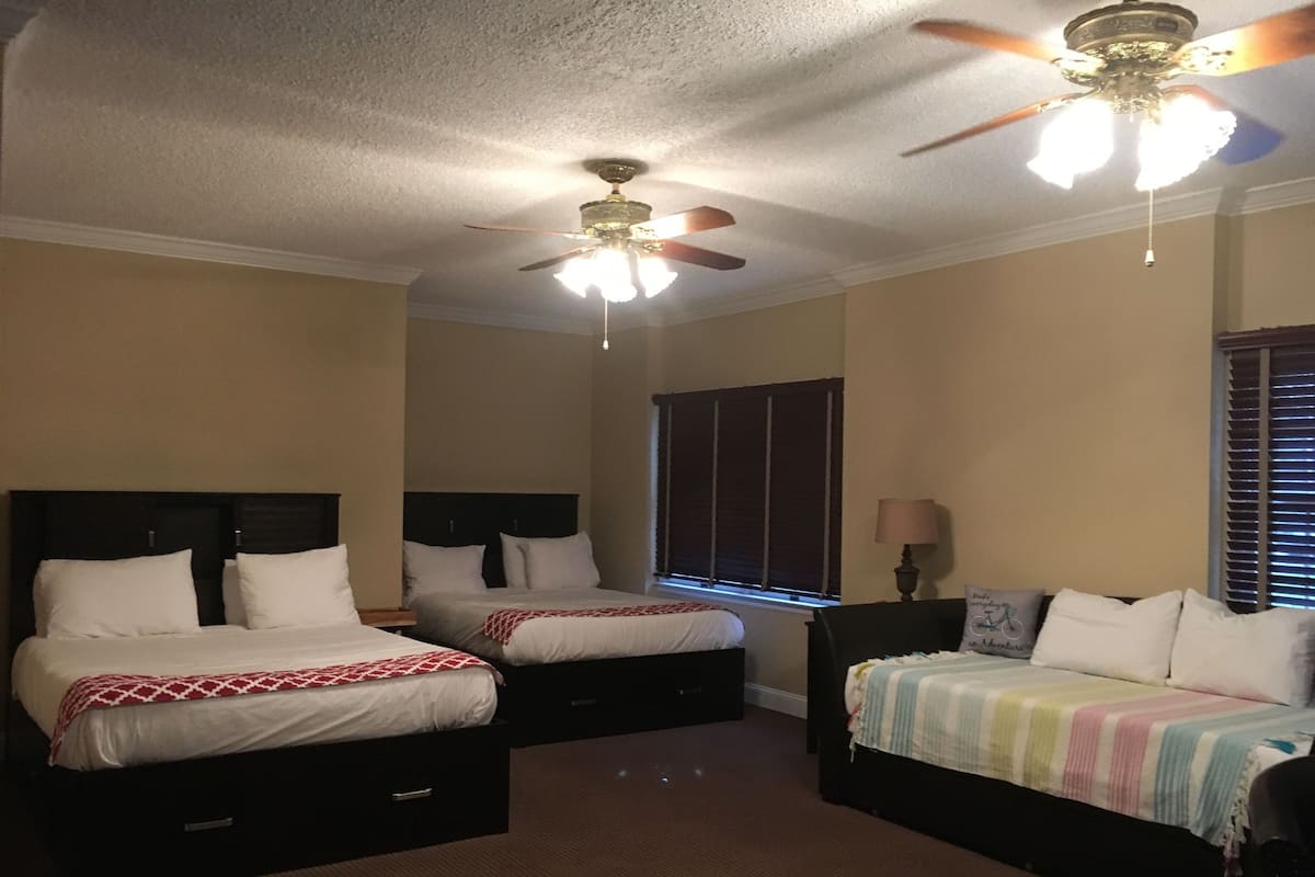 A hotel room with two beds, a ceiling fan, a window with blinds, and a lamp.