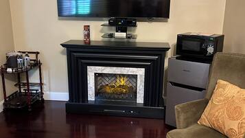 Una sala de estar con una televisión de pantalla plana sobre la chimenea, una cafetera y un microondas en un mueble.