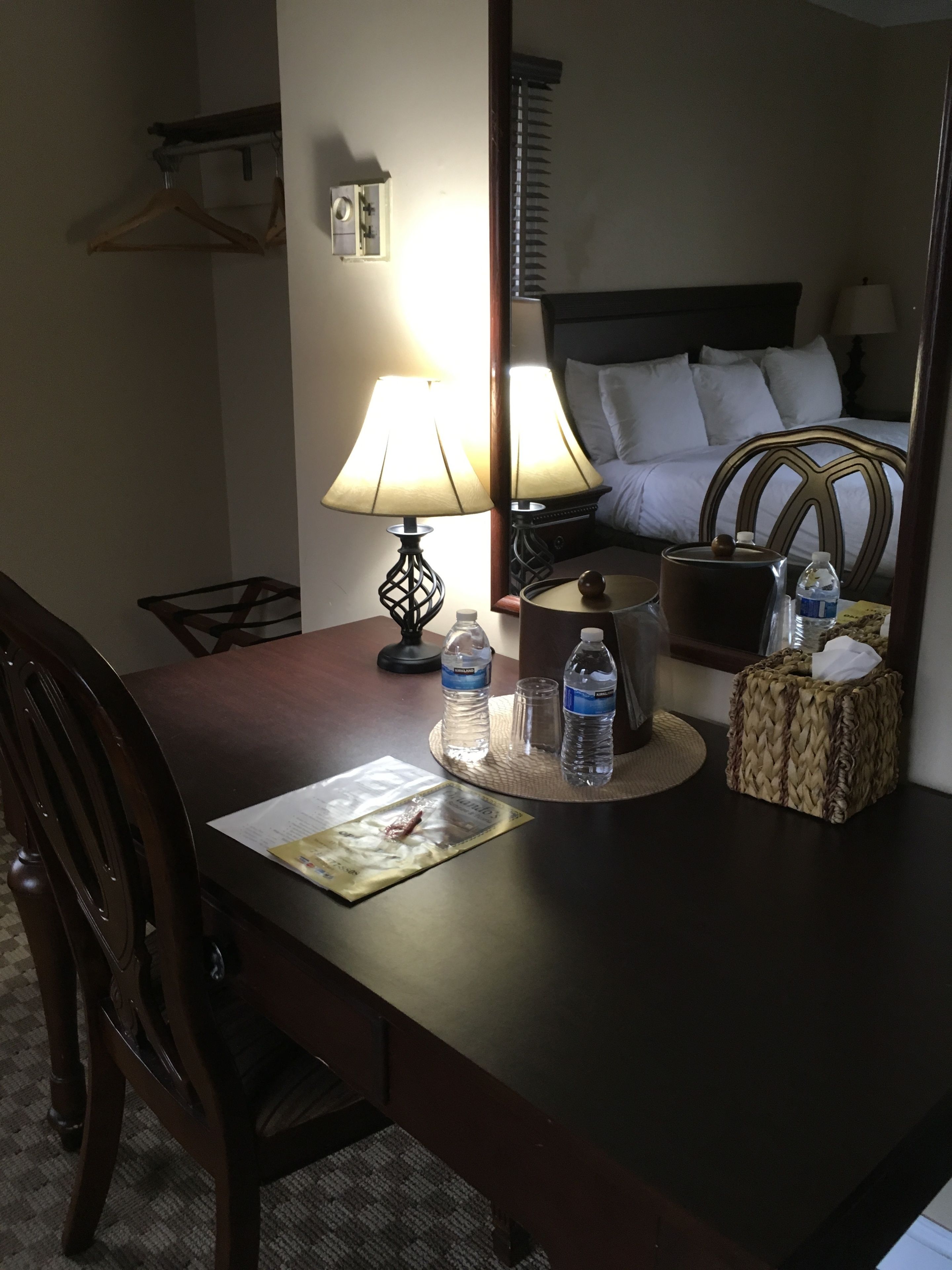 Une chambre d’hôtel avec un bureau en bois, une lampe, une bouteille d’eau, une boîte de mouchoirs et un lit recouvert de draps blancs.