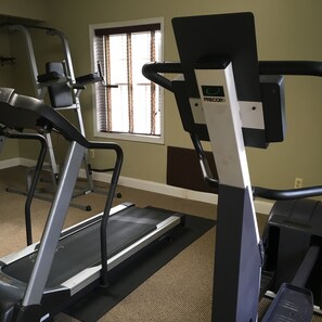 Un gimnasio con cintas de correr, bicicletas estáticas y un ventanal con persianas.