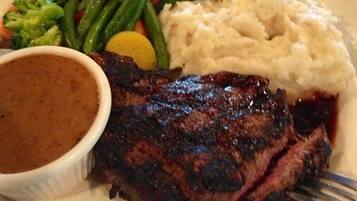 A plate with a steak, mashed potatoes, green beans, carrots, and a gravy bowl.