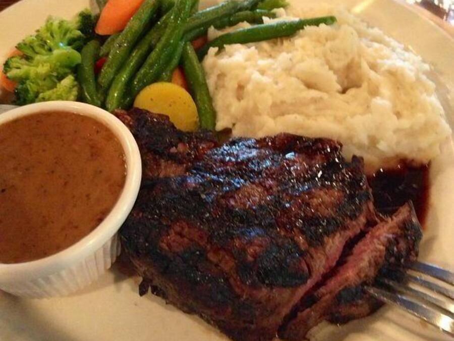 A plate with a steak, mashed potatoes, green beans, carrots, and a gravy bowl.