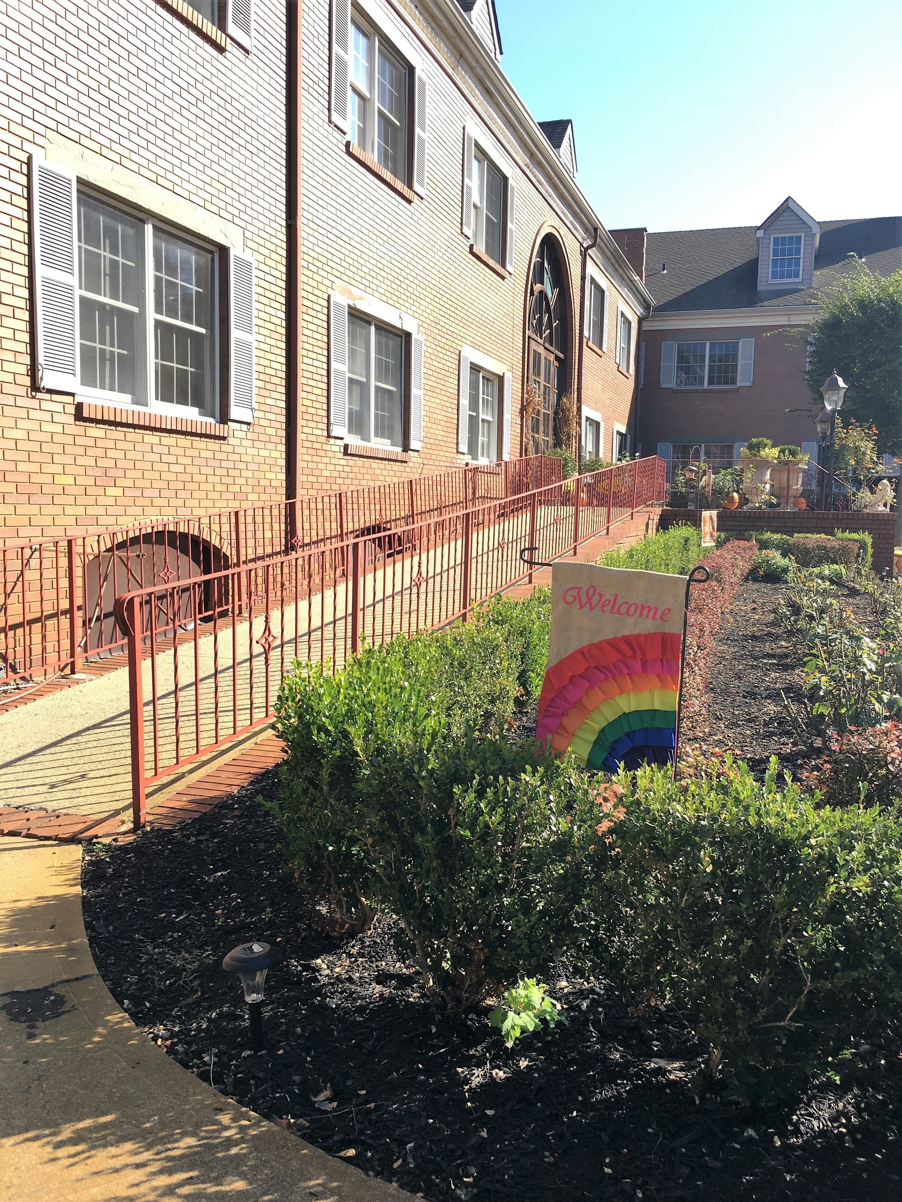 A brick building with a red metal fence, a rainbow flag, and a garden area.