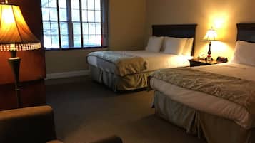 A hotel room with two beds, a chair, a nightstand with a lamp, and a window with blinds.