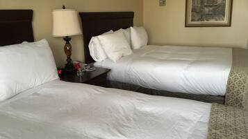 A hotel room with two beds, a bedside table with a lamp, a phone, and a framed picture on the wall.