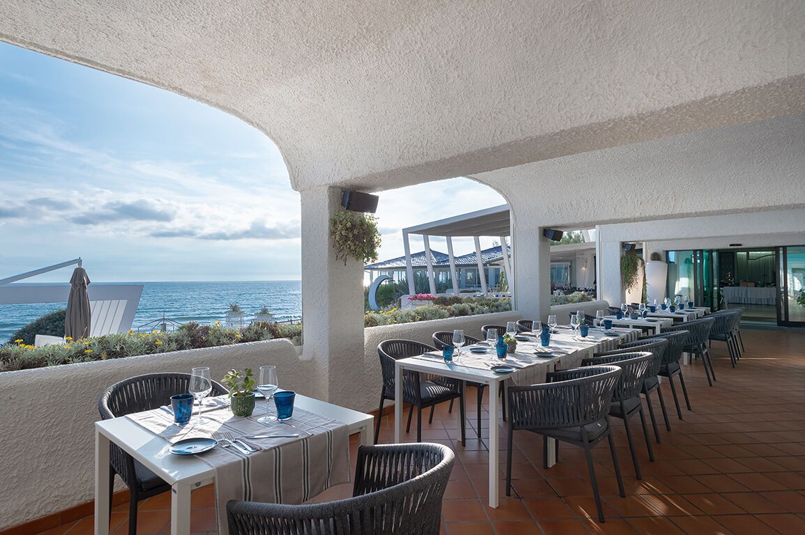 An outdoor dining area with tables and chairs, overlooking the sea.