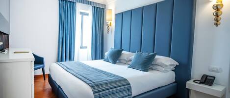 A modern hotel room with a large bed, a desk, and a phone on a nightstand.