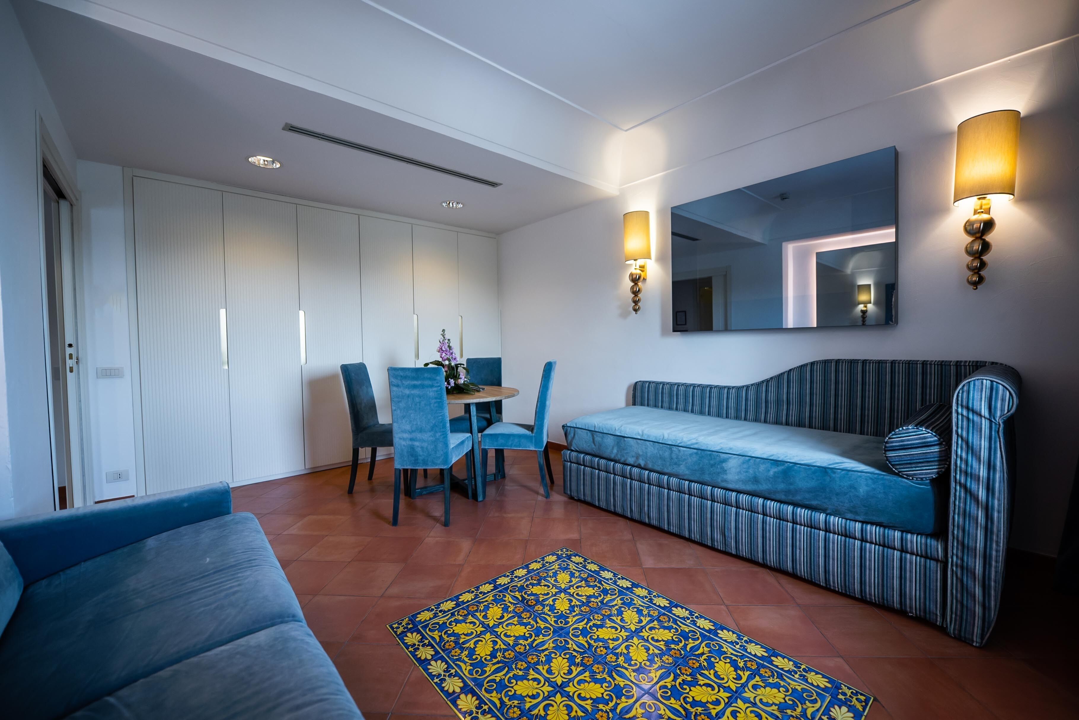 A modern living room with a sofa, a dining table with chairs, a patterned rug, and wall-mounted lighting.
