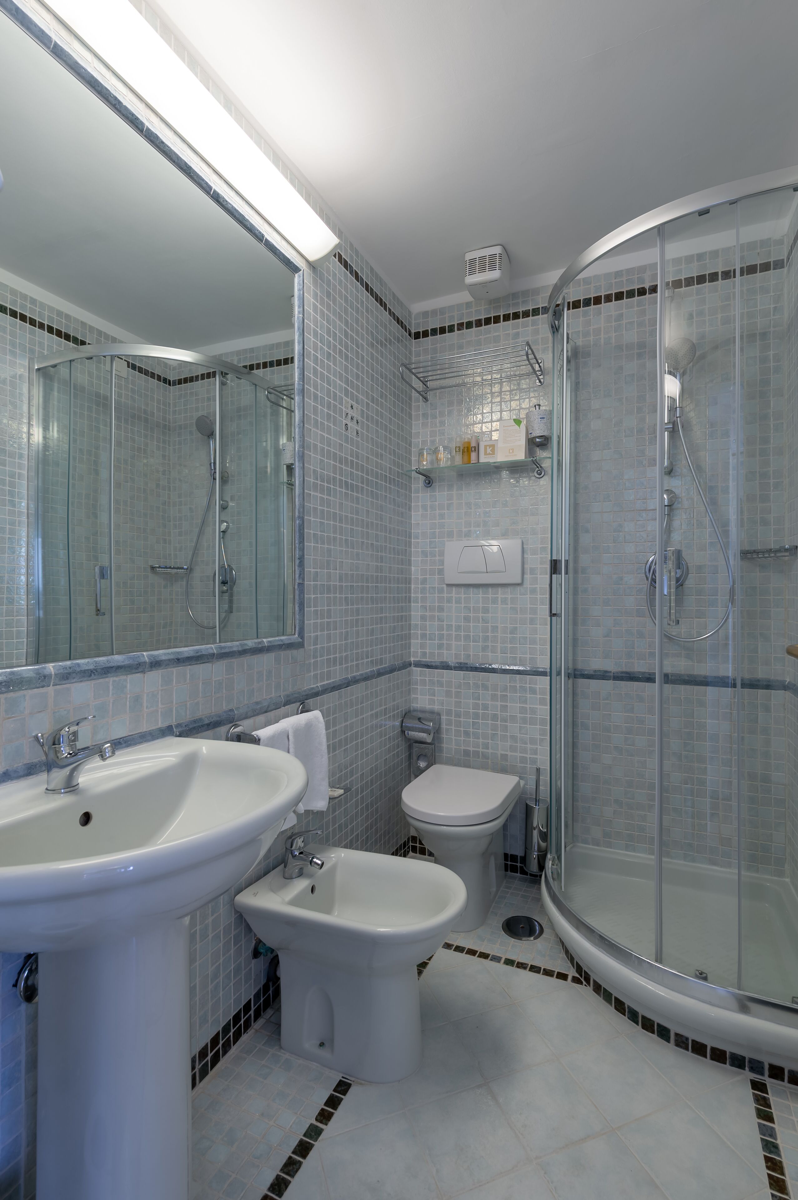 A bathroom with a sink, bidet, toilet, and a glass-enclosed shower.