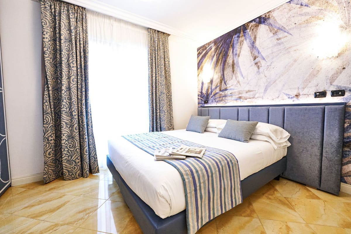 Une chambre à coucher avec un lit, des rideaux à motifs, une tête de lit et une œuvre d’art murale.