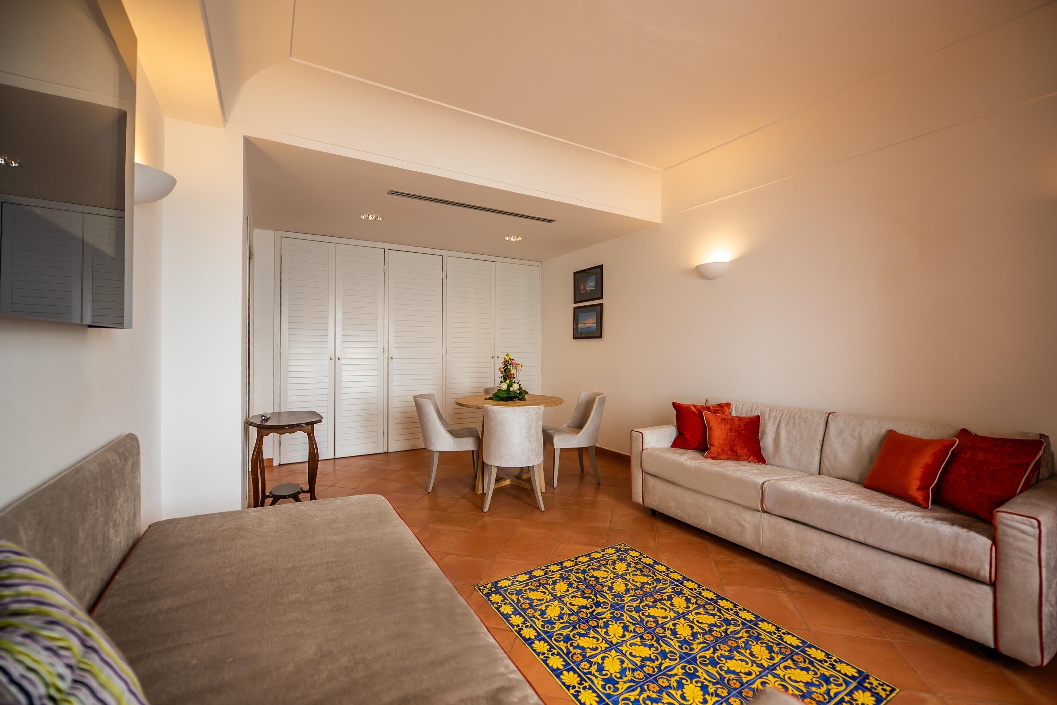 A modern living room with a sofa, a dining table with chairs, and a patterned rug.