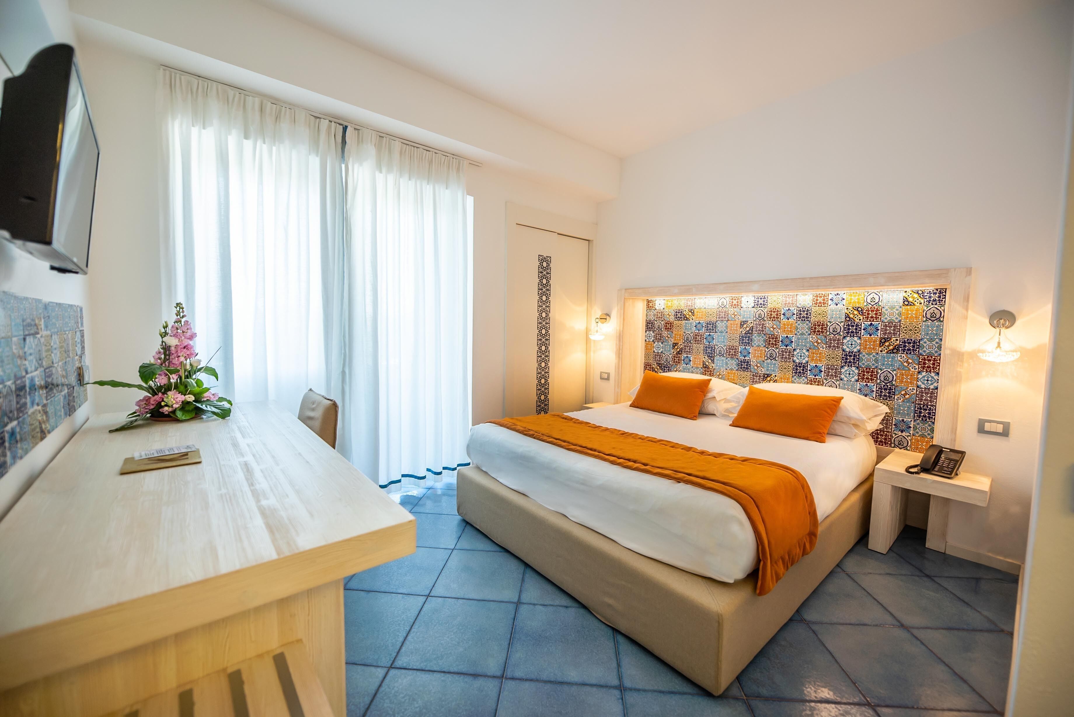 A hotel room with a bed, bedside table, and a desk with a chair.