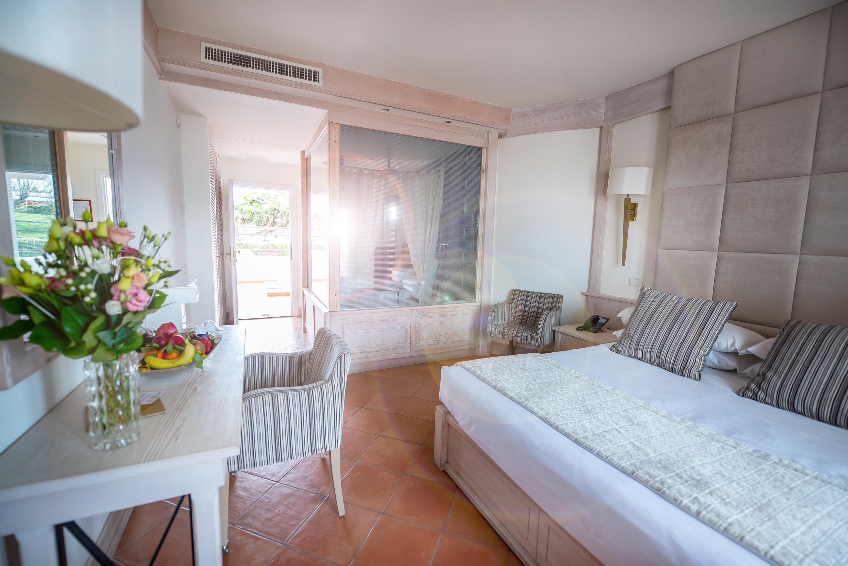 Una habitación de hotel con cama, mesita de noche, silla y ventana con cortinas.