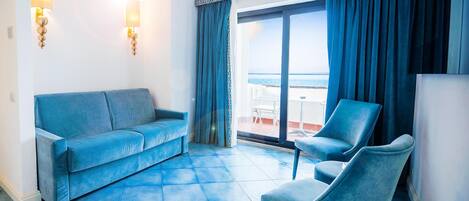 A room with a blue sofa, a blue armchair, and a large window with a view of the sea.