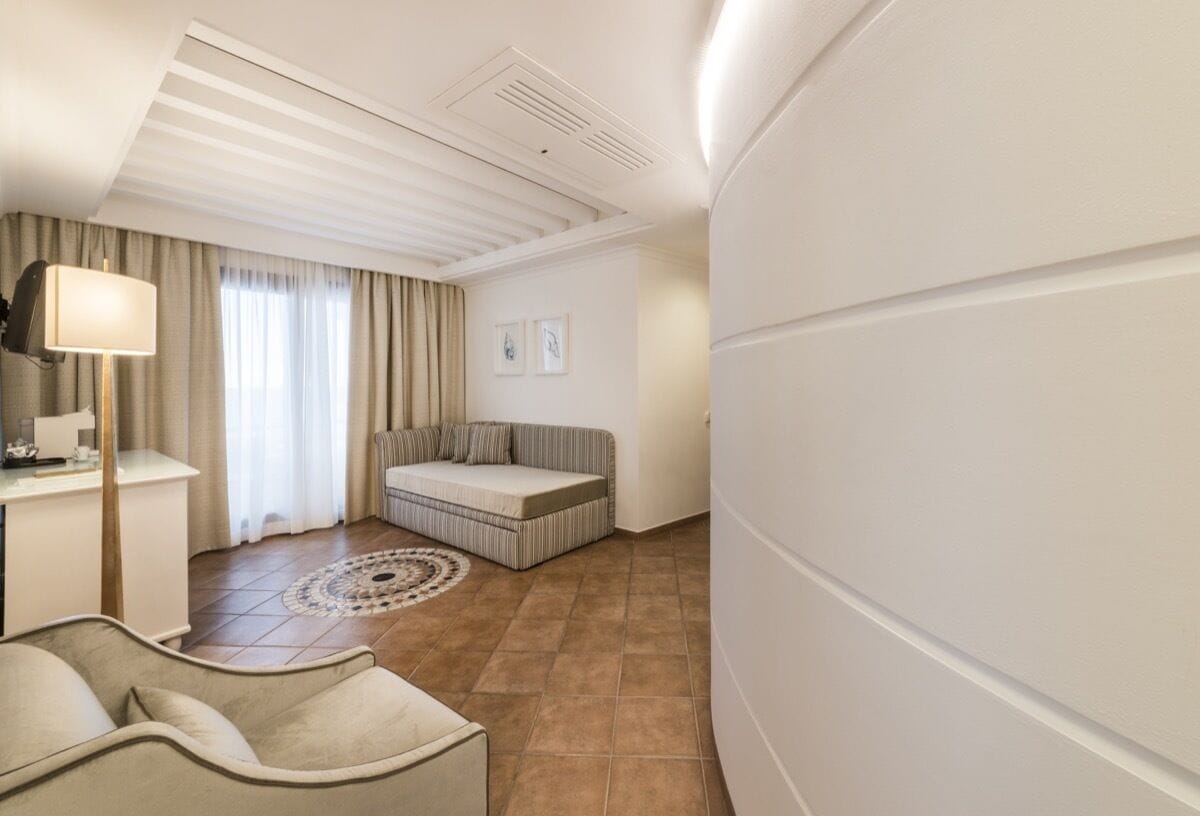 A hotel room with a sofa, a small table, a lamp, and a window with curtains.