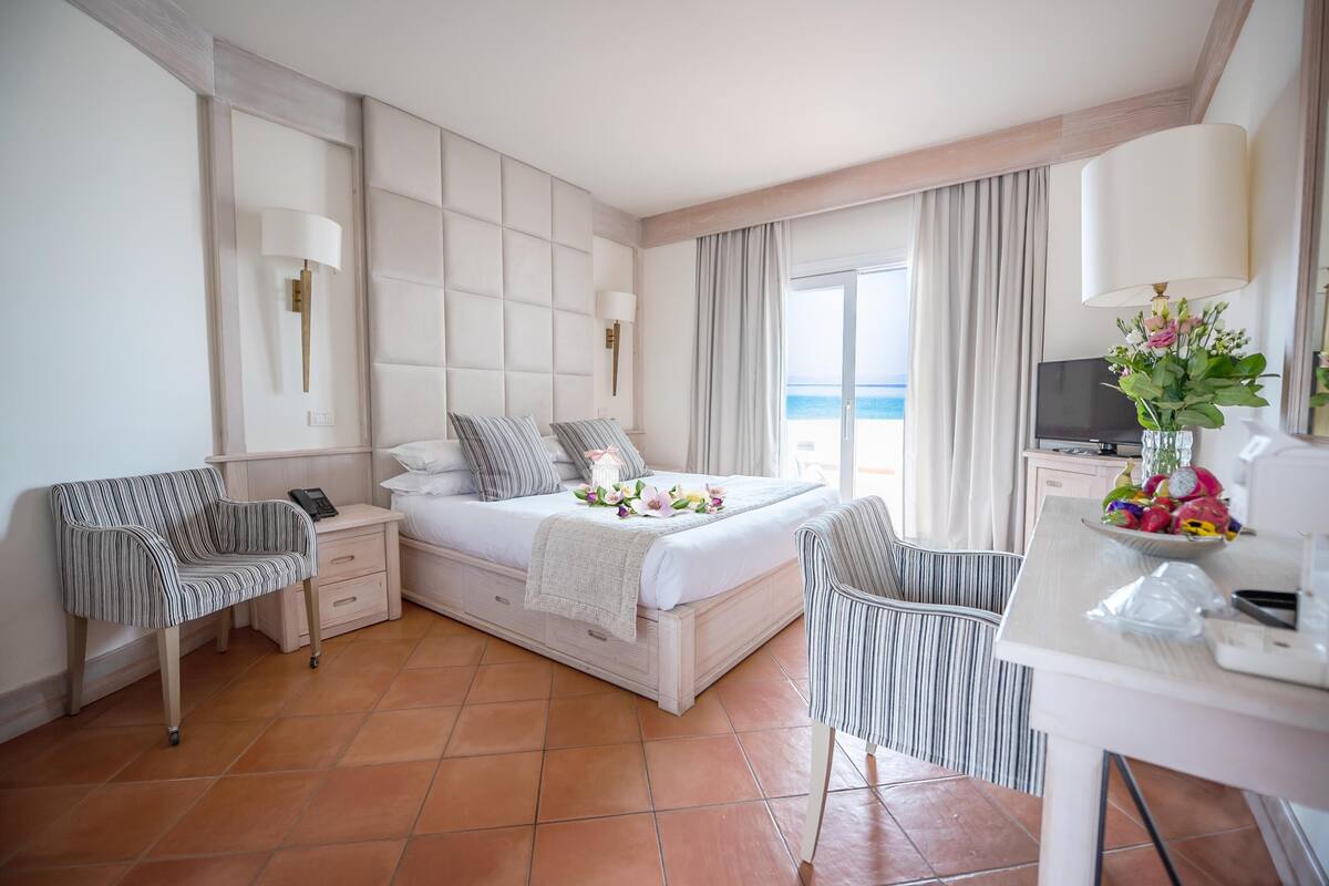 Une chambre d’hôtel avec un grand lit, un bureau avec une chaise, une télévision et une vue sur l’océan.
