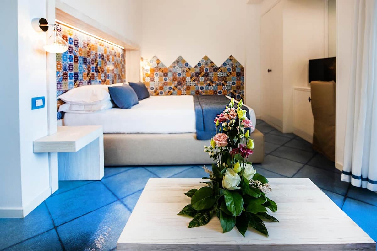 Une chambre d’hôtel moderne, équipée d’un lit, d’une table de chevet, d’un mur décoratif et d’un arrangement floral posé sur une table basse.