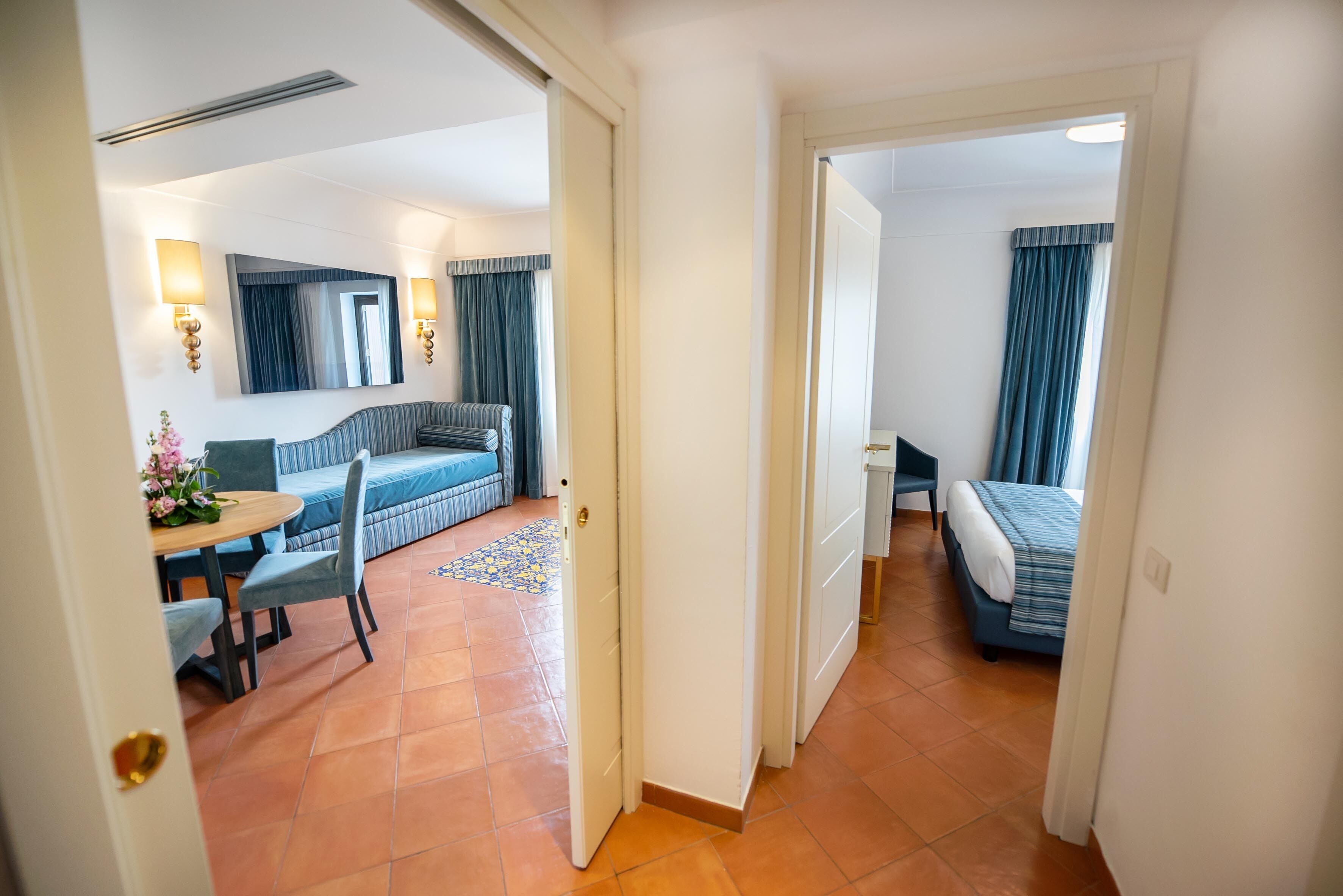 A hotel room with a bed, a sofa, a dining table with chairs, and a small kitchen area.
