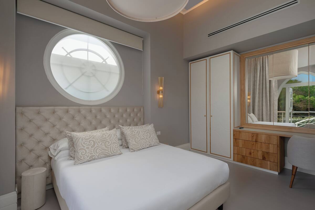 Une chambre à coucher avec un grand lit, une fenêtre ronde, une armoire et un bureau avec une chaise.