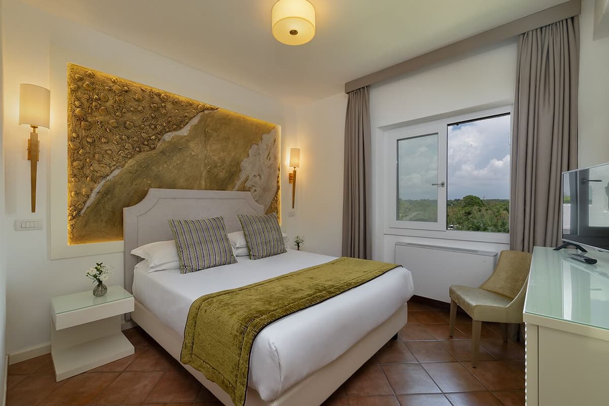 Une chambre d’hôtel avec un grand lit, un bureau avec une télévision, une fenêtre avec des rideaux et une œuvre d’art accrochée au mur.