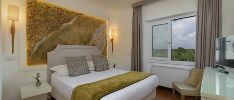 A hotel room with a large bed, a desk with a television, a window with curtains, and a wall-mounted artwork.