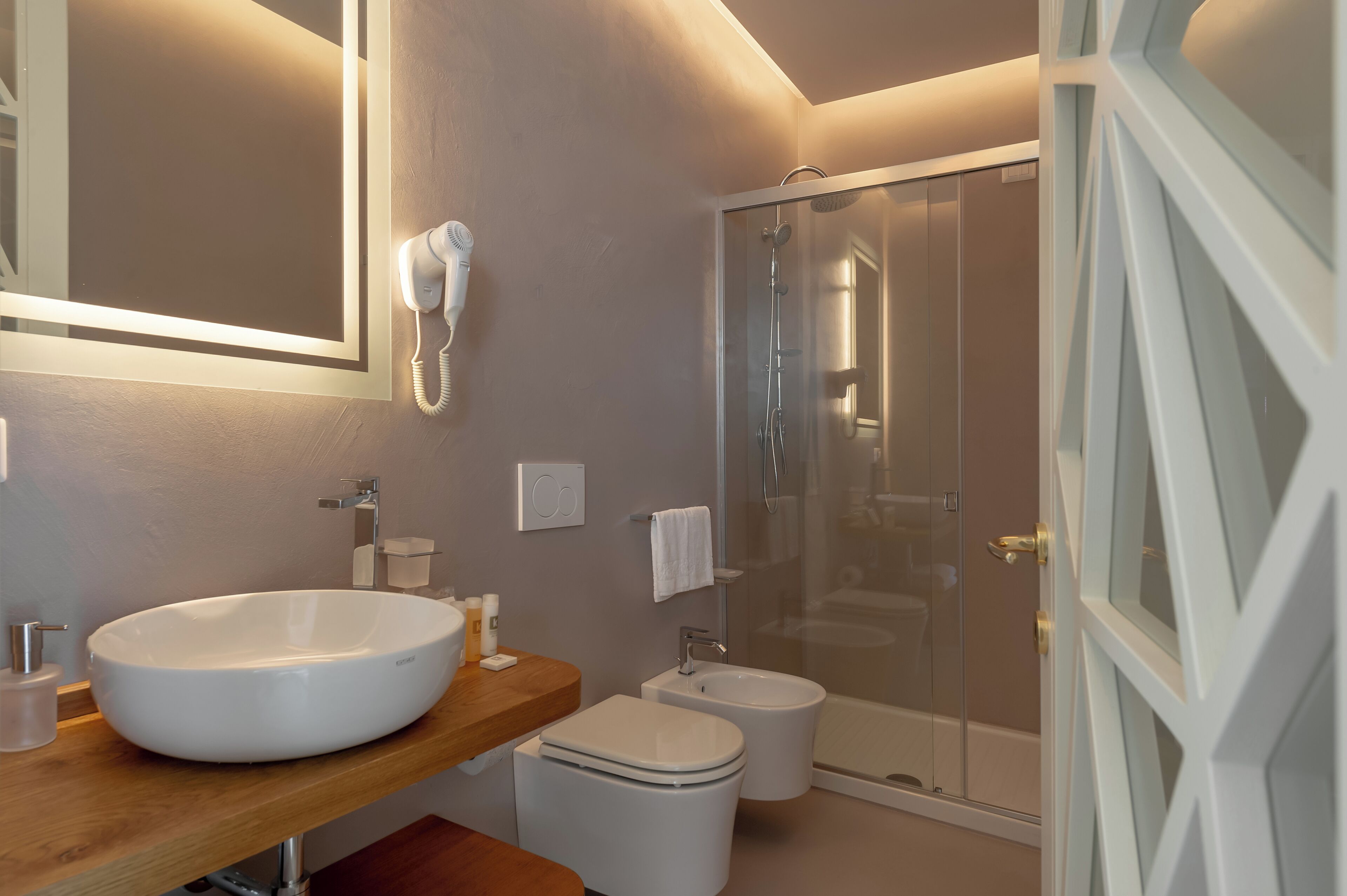 Een moderne badkamer met een groot wit wastafel, een bidet, een douche met glazen wanden en een wastafelmeubel met spiegel.
