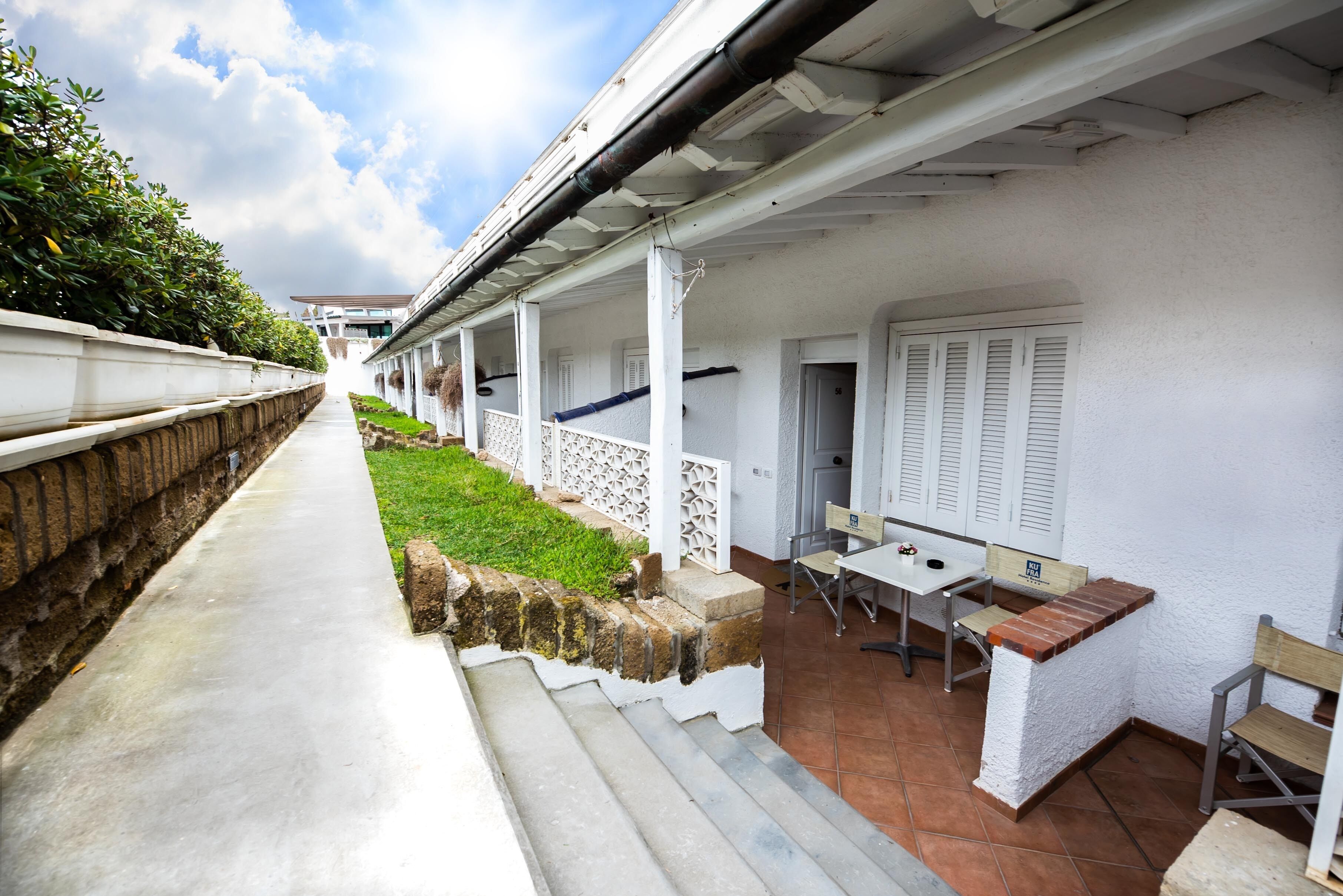 A covered outdoor patio with a table and chairs, a brick wall, and a grassy area.