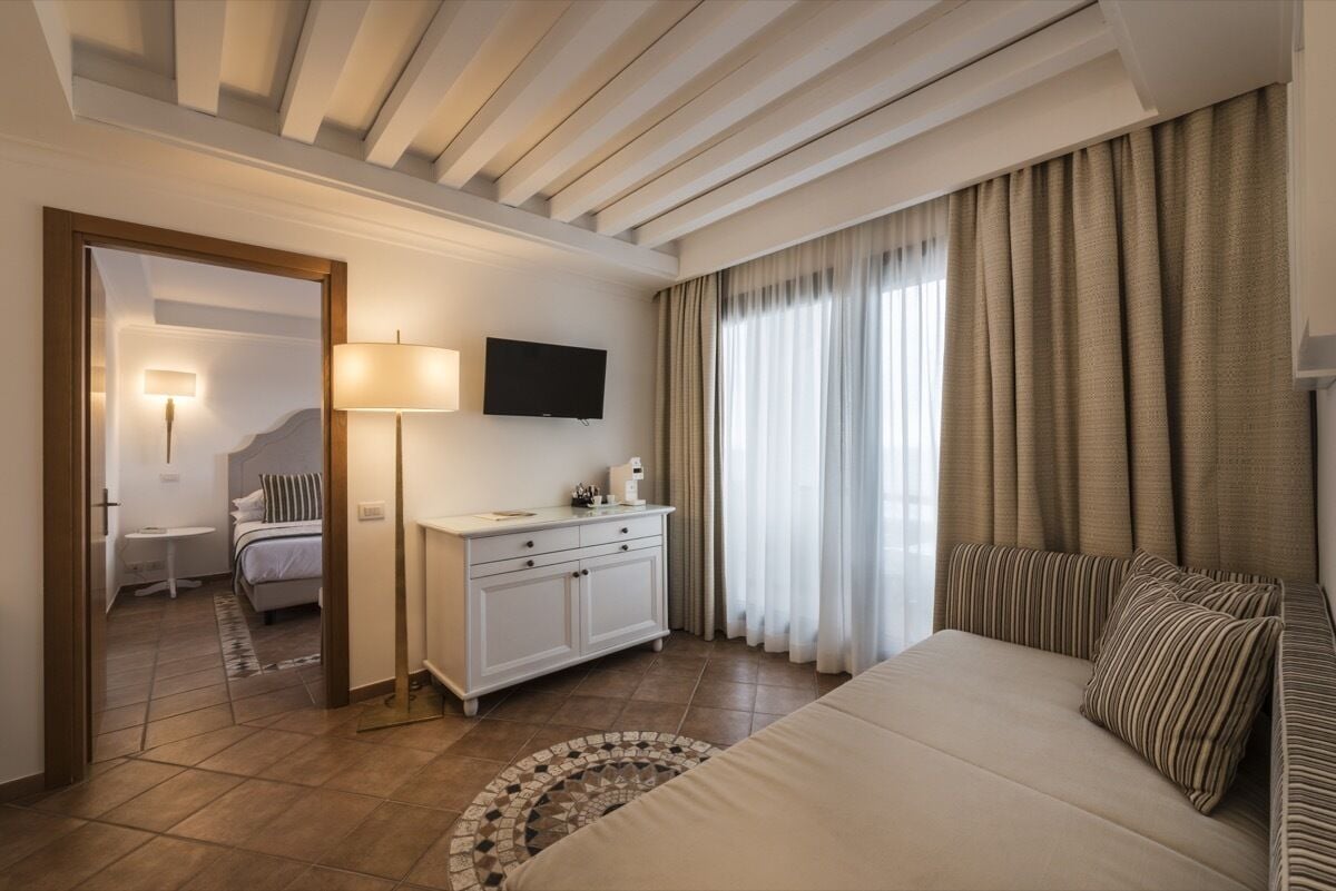 Een hotelkamer met een bed, een bureau met lamp, een televisie en uitzicht op de omgeving door grote ramen.