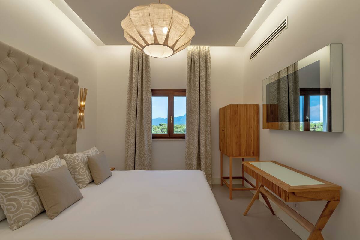 Une chambre avec un grand lit, un bureau en bois, un miroir et une vue sur l’extérieur.