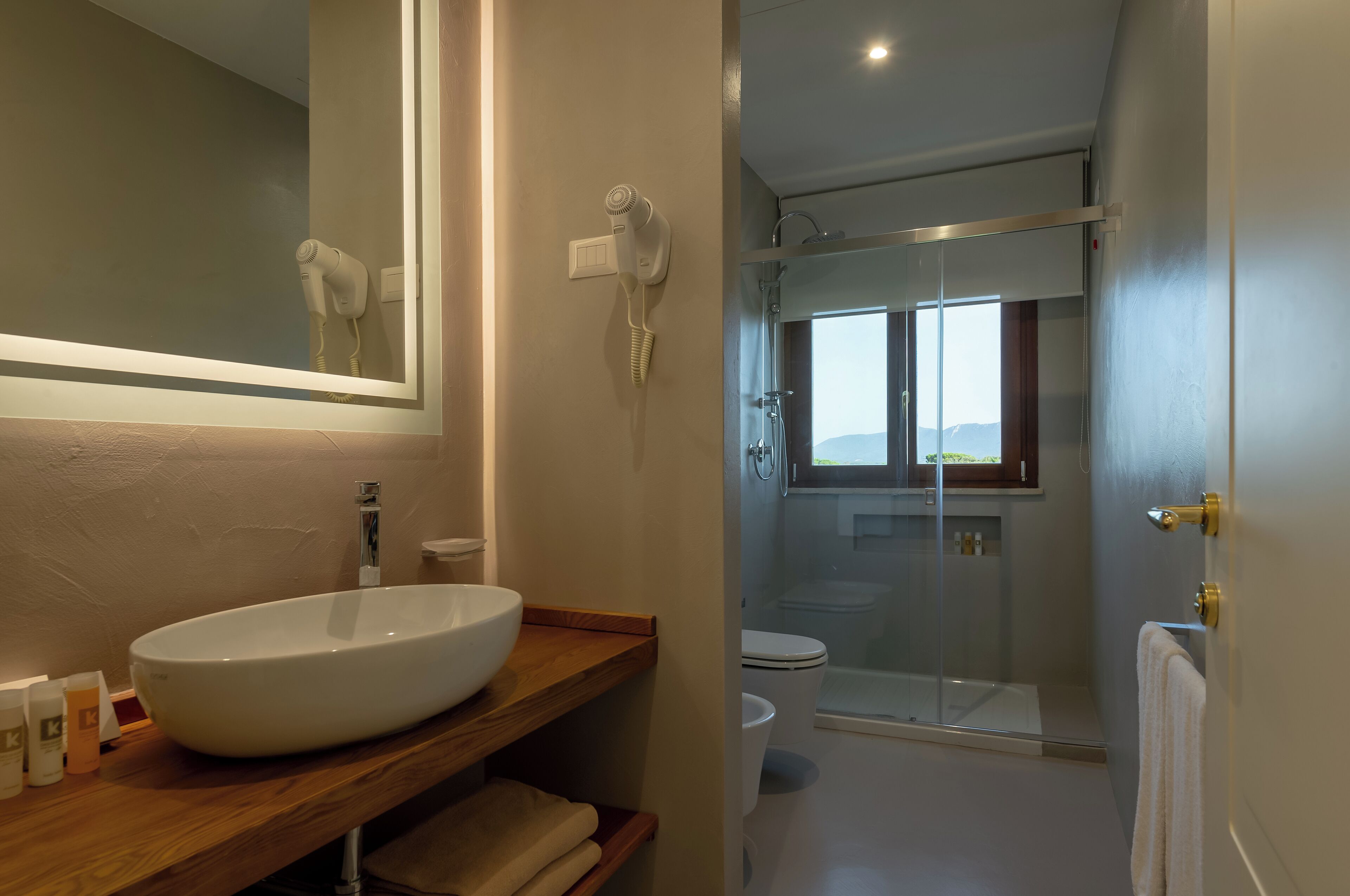 A modern bathroom with a large mirror, a white sink, a hairdryer, and a glass-enclosed shower.