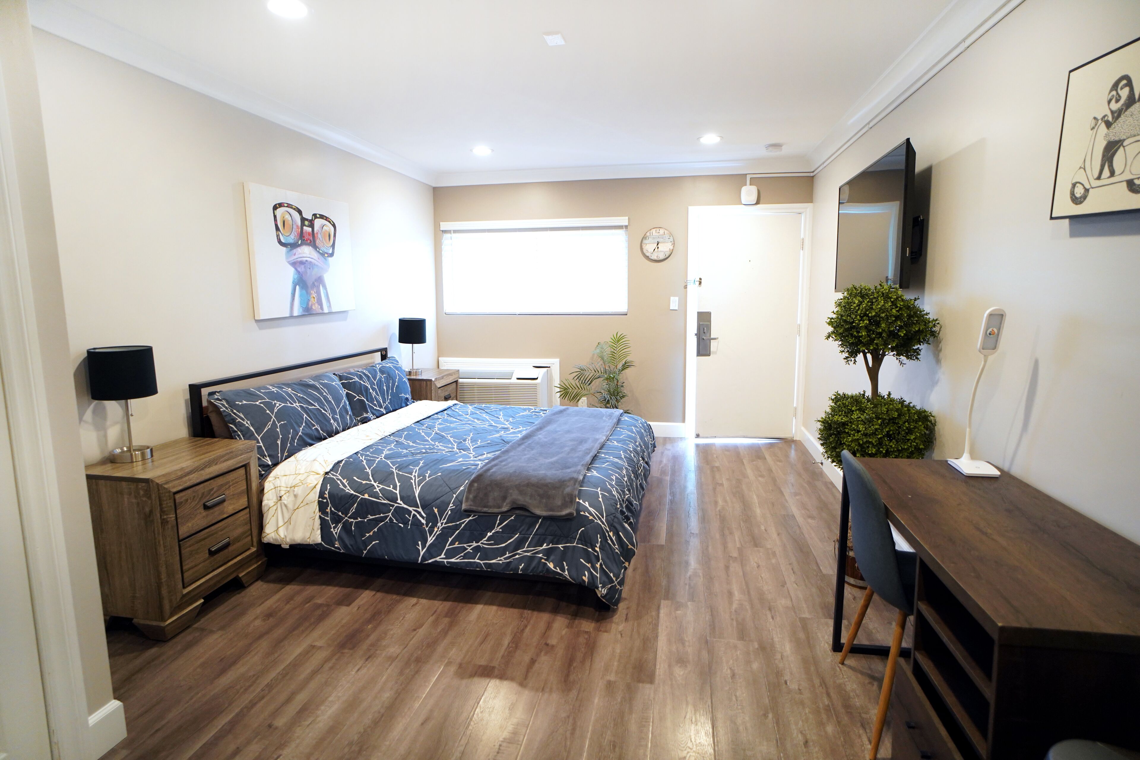 A bedroom with a bed, bedside table, lamp, and a desk with a chair.