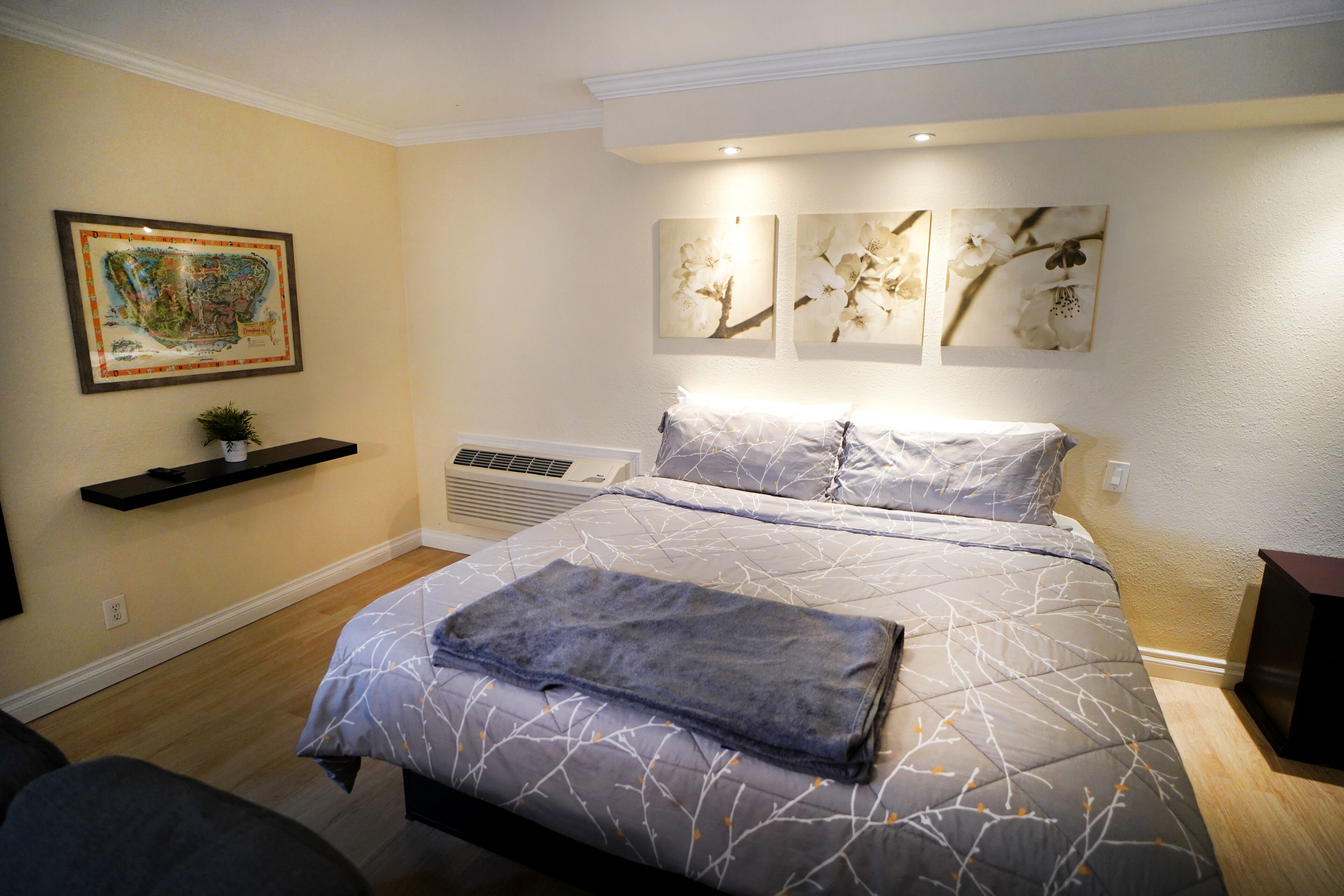 A bedroom with a bed, a wall-mounted air conditioner, and three framed artworks.