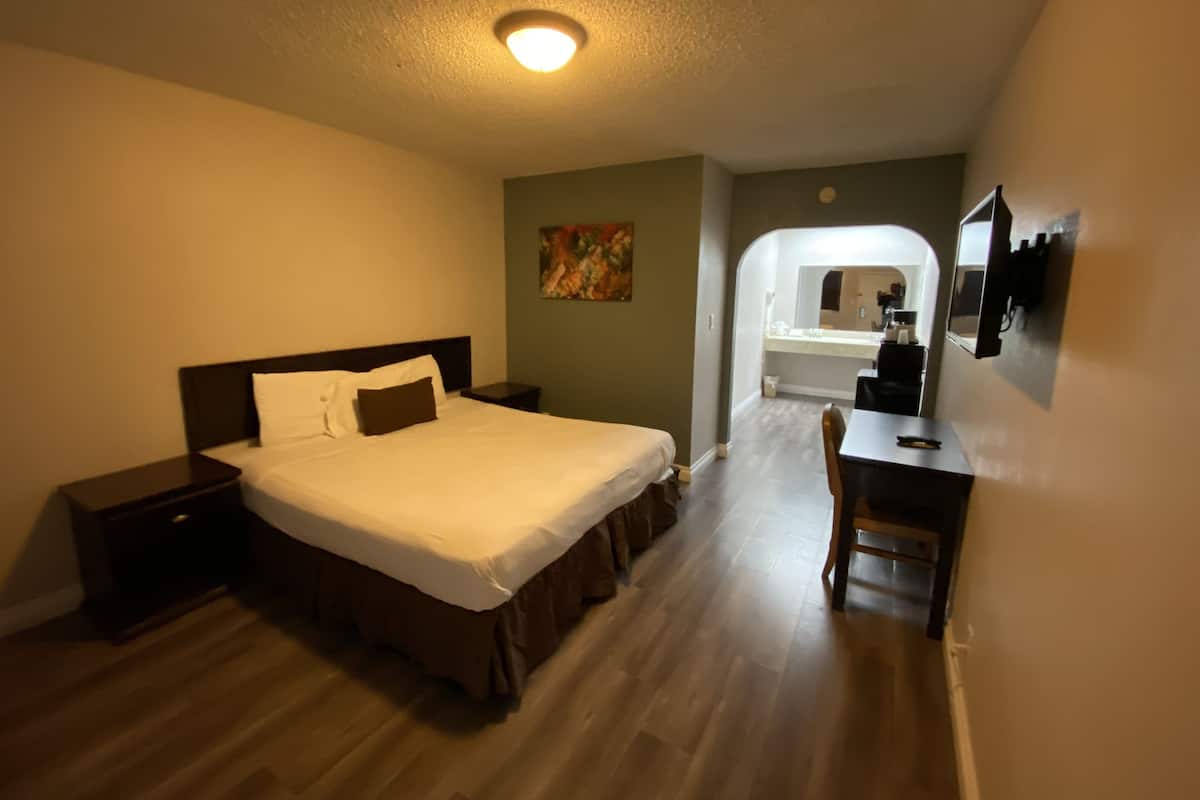 A hotel room with a bed, bedside table, desk, chair, and a bathroom visible through an archway.