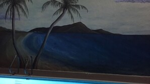 Une piscine ornée d’une fresque représentant des palmiers et des montagnes en arrière-plan.