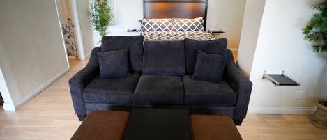 A modern living room with a dark grey sofa, a small black coffee table, and a wooden floor.