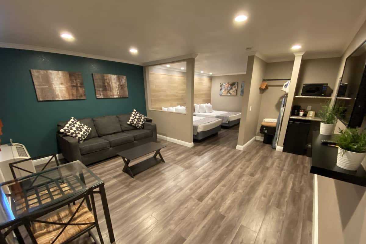 A modern living room with a sofa, coffee table, and a dining area with a glass table. There is a kitchenette with a refrigerator and a microwave.