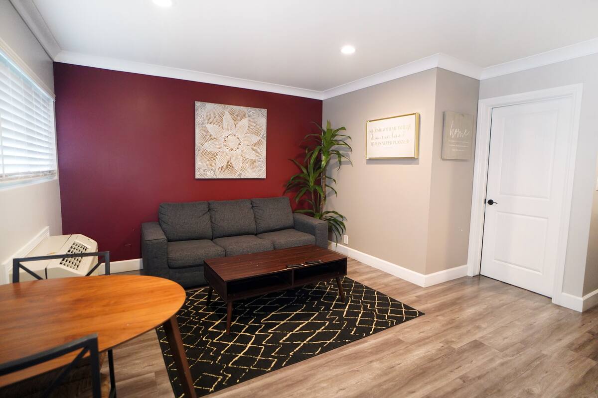 A living room with a grey sofa, a wooden coffee table, a black and gold rug, and a white door.