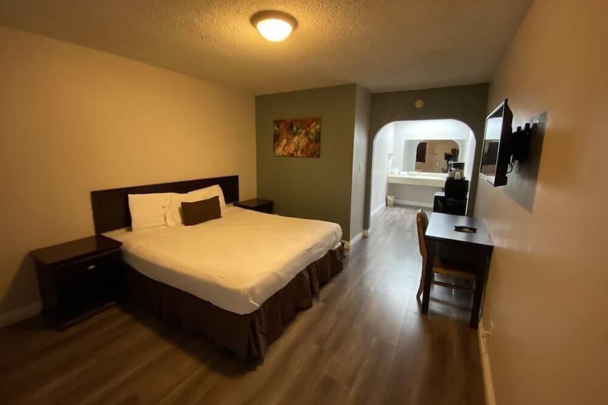 Habitación de hotel con cama, mesita de noche, escritorio, silla y baño visible a través de un arco.