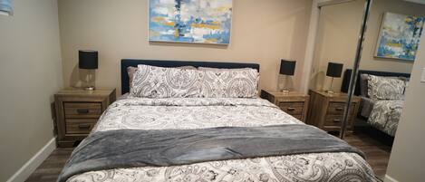 Un dormitorio con una cama grande, dos mesitas de noche con lámparas, un espejo y una obra de arte abstracta en la pared.