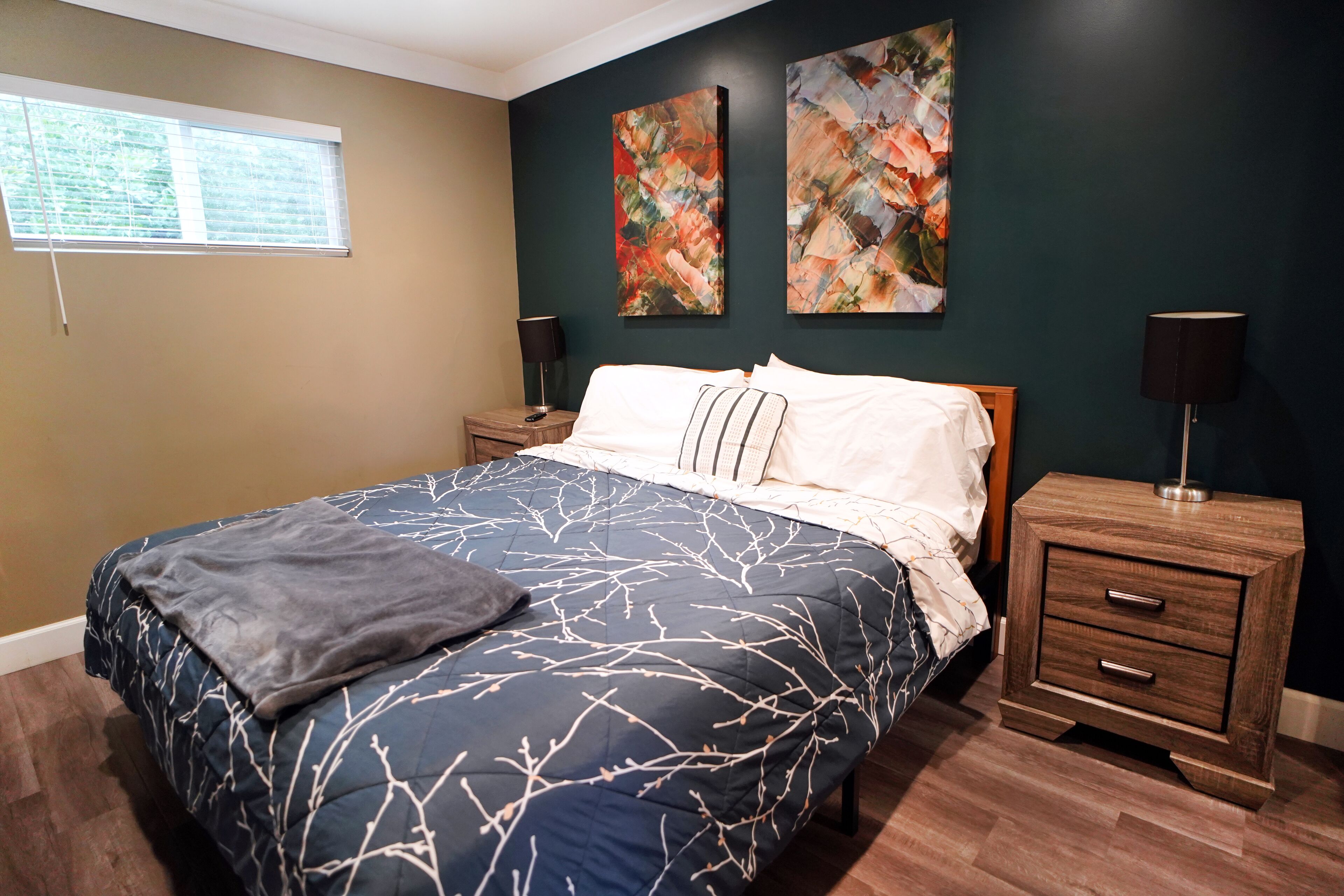 Un dormitorio con una cama grande, dos mesitas de noche, un ventanal y una obra de arte abstracta en la pared.