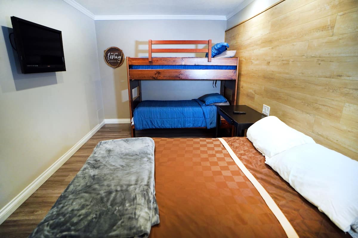 A room with a bunk bed, a flat bed, a television, and a small table.